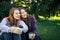 Attractive lesbian couple drinking coffee on grass in park with copy space. Girls sit close to each other, look in one side and