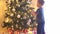 Attractive little boy decorating Christmas tree with balls and lights. Kid preparing for the New Year at home.