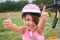 Attractive little cyclist giving thumbs up. Happy joyful little girl with bicycle on the background gesturing thumb up