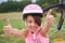 Attractive little cyclist giving thumbs up. Happy joyful little girl with bicycle on the background gesturing thumb up