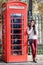 Attractive Lonodn traveler woman stands next to a classic, red telephone booth