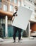 Attractive man holding blank canvas at the street and looking at the viewer.