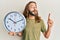 Attractive man with long hair and beard holding big clock smiling with an idea or question pointing finger with happy face, number