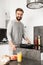 Attractive man with short brown hair and beard cooking alone breakfast with eggs and vegetables in home kitchen, using frying pan