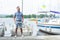 Attractive man stands at the nose of white boats on pier at river marina. Young yachtsman near of own boat