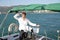 Attractive man in white stands at the helm of a yacht at sea and looks at the horizon with his hand raised Sailing, tourism travel