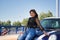 Attractive mature woman in black transparent shirt and jeans, smiling very happy, leaning on small sporty car. Concept maturity,