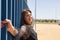 Attractive mature woman in transparent black shirt and jeans, with open arms, posing clutching a blue fence in seductive attitude