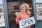 attractive middle aged small business owner holding sign open and smiling