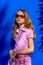 Attractive model Barbie style girl wearing sunglasses, pink tee-shirt and shorts with long hair on blue backdrop