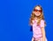 Attractive model Barbie style girl wearing sunglasses, pink tee-shirt and shorts with long hair on blue backdrop