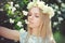 Attractive modest young girl with blonde with jasmine flowers wreath on head long hair and natural make-up in white dress outdoors