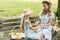 attractive mother and adorable daughter in straw hats holding hands and sitting on bench with fruits in wicker
