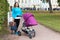 Attractive mother with baby stroller walks in summer park near beauty palace, excursion in Russian historical places, copy space