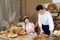 An attractive new saleswoman describes wooden plates with prices for individual types of bread under the supervision of