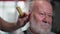 attractive older man with a gray beard doing a hair trimmer in a mens salon by a modern barber, close-up