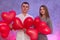 Attractive pair with red air balloons smiling in studio. Couple in love