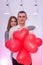 Attractive pair with red air balloons smiling in studio. Couple in love