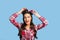 Attractive pinup lady in retro outfit tying bow on her head, styling her hair on blue studio background