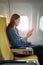 Attractive portrait of Asian woman sitting at window seat in economy class using mobile phone during plane flight