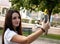 Attractive red haired brunette holding a smartphone taking a selfie smiling in a public park. Young traveler in a .white t shirt
