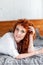 Attractive red-haired curly girl lies resting on the bed