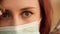 Attractive redhead woman wears surgical mask and looks away