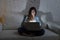 Attractive relaxed woman at home sitting happy on couch using laptop in dark evening