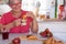 Attractive retired senior woman enjoying breakfast at home with croissant and cappuccino. Strawberries on the table