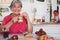 Attractive retired senior woman enjoying breakfast at home with croissant and cappuccino. Strawberries on the table