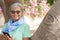 Attractive senior woman white haired looking at camera wearing sunglasses and fashion scarf using smart phone and smiling.