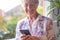 Attractive senior woman at the window holding mobile phone while writing a message. Smiling gray-haired senior enjoying technology