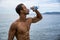 Attractive shirtless muscleman on the beach drinking water