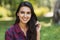 Attractive shot of happy young brunette Caucasian female smiling and wearing plaid shirt against nature background in the park.