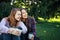 Attractive sisters drinking coffee on grass in park with copy space. Girls sit close to each other, look in one side and fun