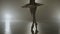 Attractive skinny ballerina silhouette in white tutu outfit dancing while warming up in a professional dark studio -