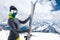An attractive slender woman skier stands without a jacket high in the mountains and holds her skis against the
