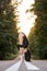 Attractive slim ballerina posing with head bowed on road, in coniferous forest.