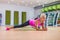 Attractive slim blonde middle-aged woman doing planking or stretching exercise on mat against colorful sport equipment