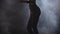 Attractive slim woman dances in dark smoky studio