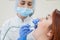 An attractive smiling female doctor in white uniform examines a red-haired female patient. Dentist produces treats teeth