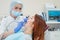 An attractive smiling female doctor in white uniform examines a red-haired female patient. Dentist produces treats teeth