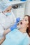 An attractive smiling female doctor in white uniform examines a red-haired female patient. Dentist produces treats teeth