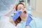 An attractive smiling female doctor in white uniform examines a red-haired female patient. Dentist produces treats teeth