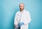 Attractive smiling man bald bearded doctor puts on rubber medical gloves looking at camera isolated on blue background