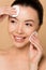 Attractive smiling nude asian woman removing makeup from face with cotton pads