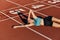Attractive smiling sporty girl in sportswear happily lying on runner track while resting after workout on stadium