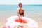Attractive smiling woman is calling her boyfriend into the sea. Couple is holding doughnut inflatable ring. Follow me concept