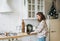 Attractive smiling woman with curly hair in plaid shirt with laptop near window at bright kitchen at home