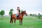 Attractive sport cowgirl horse woman with hat, holding harness, training. Horseback riding dressage, sky, grass meadow